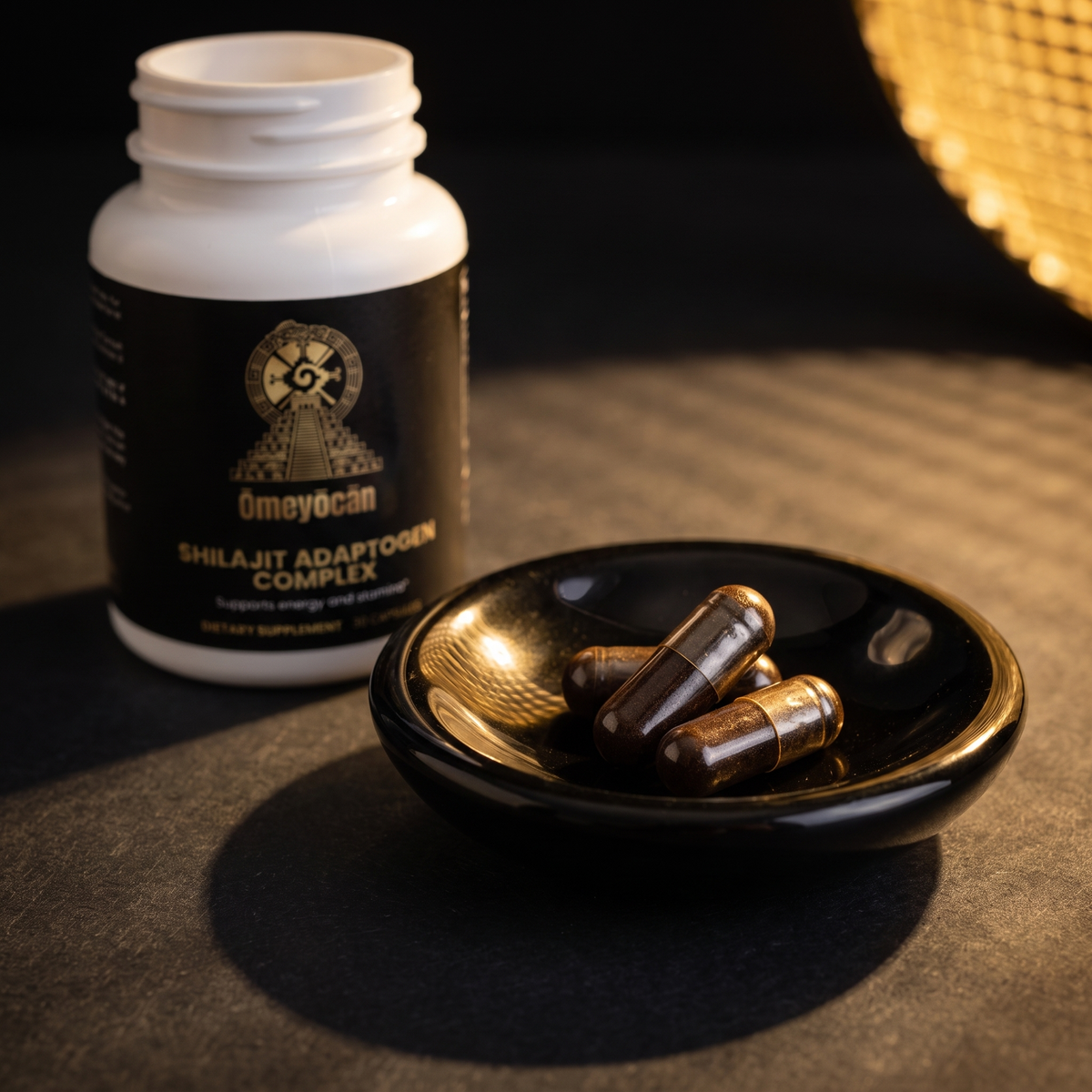 Close-up of Omeyocan shilajit capsules in an obsidian dish beside the open bottle