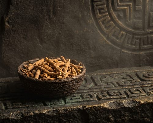 Dried ashwagandha root in a woven basket on carved basalt stone